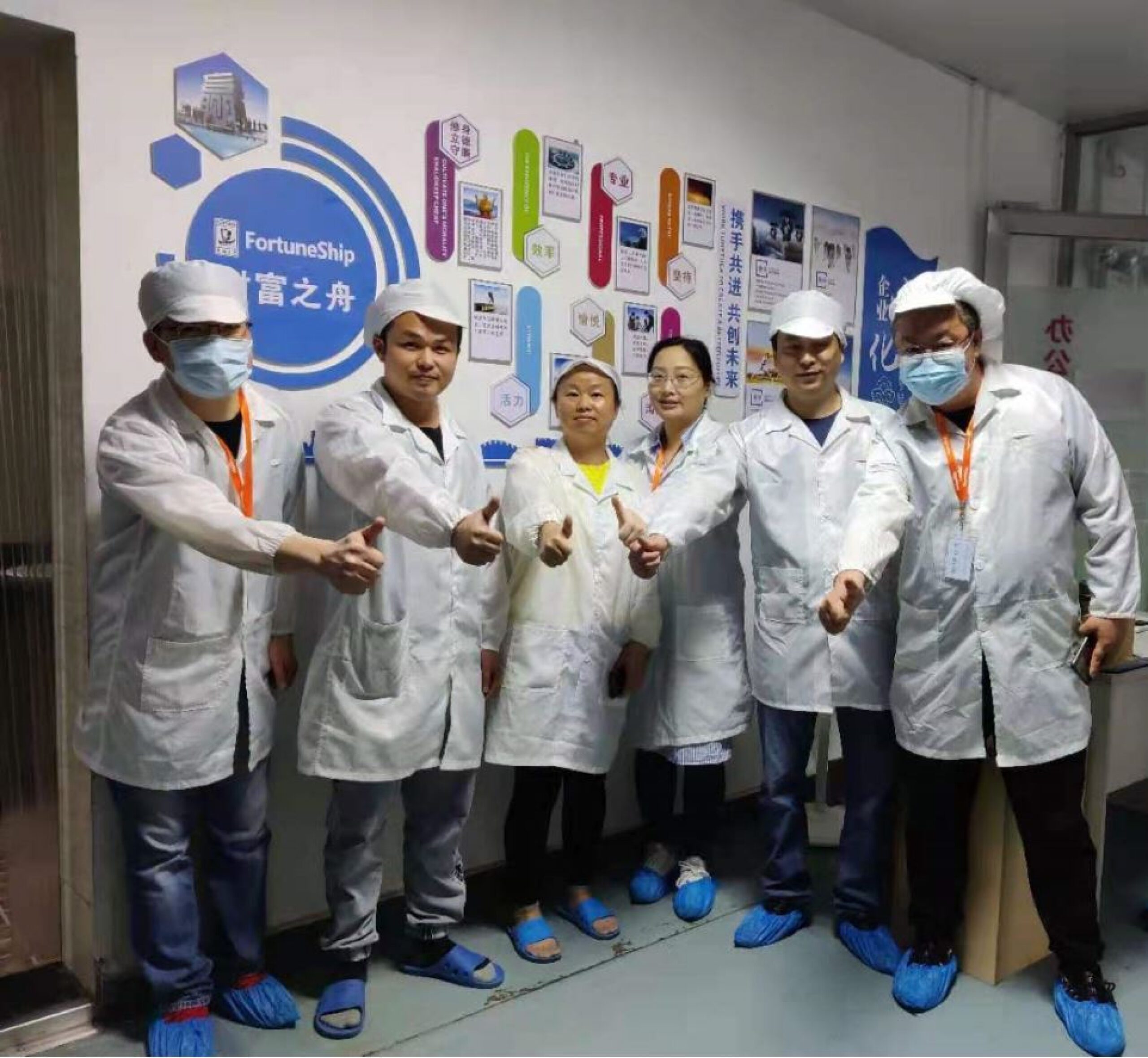 Our factory team posing in white lab coats and giving thumbs ups