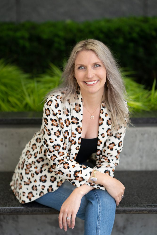 Blonde woman in leopard print blazer sitting and smiling